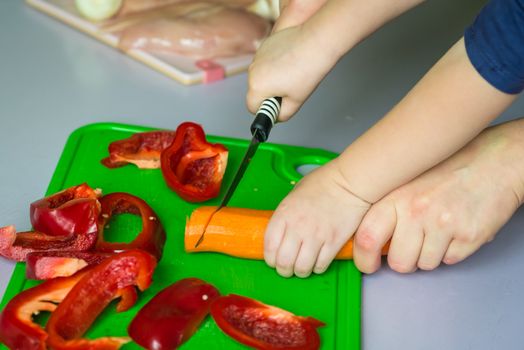 Children and mother hands cut carrot on green board