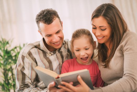 Beautiful young smiling family relaxing on sofa at living room while reading book.