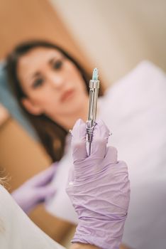 Dentist holding an injection of anesthesia. Selective focus. Focus on syringe. Female patient sitting at dental office in background.