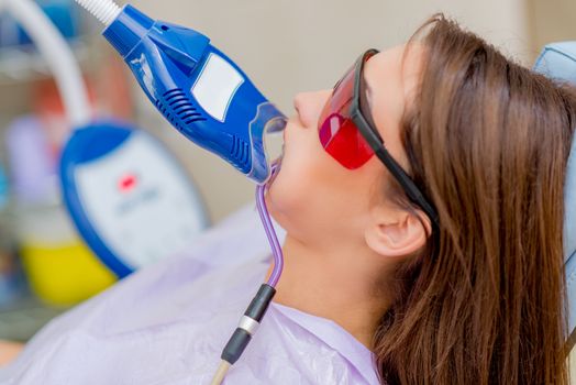 Beautiful young woman in visit at the dentist office. She is whitening teeth with ultraviolet light.