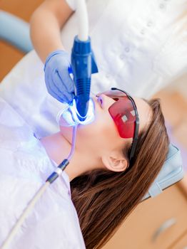 Beautiful young woman in visit at the dentist office. She is whitening teeth with ultraviolet light.