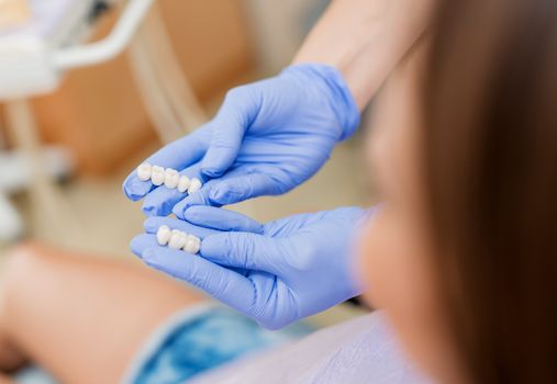 Dentist showing porcelain crowns to the patient. Close-up. Selective focus. Focus on crowns. 