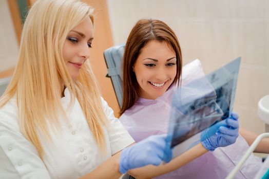 Young female dentist showing to the patient X-ray picture in she`s office. Selective focus.
