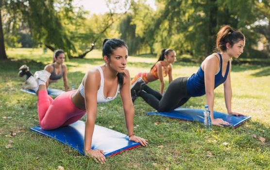 Four beautiful female friends doing push-up in the park. Selective focus. 