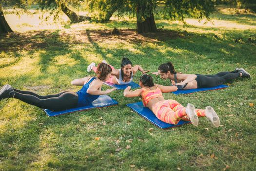 Four beautiful female friends doing plank exercise in the park. 