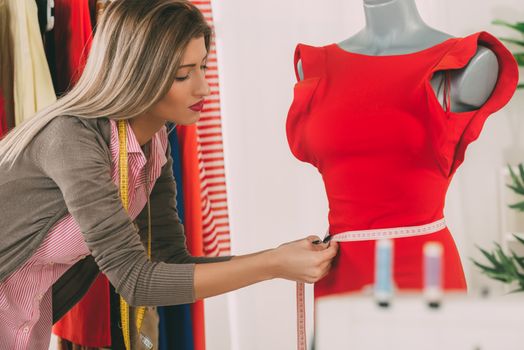 Young beautiful girl with a tape measure, takes measure of clothing which standing on a mannequin.