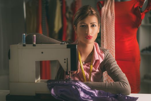 Beautiful young woman sits in front of the sewing machine and thinking. Looking at camera. Vintage concept.