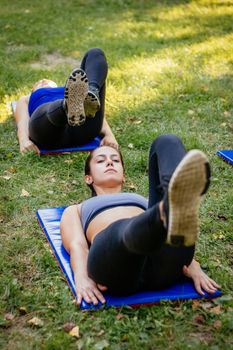 Beautiful young woman doing sit-up in the park. 