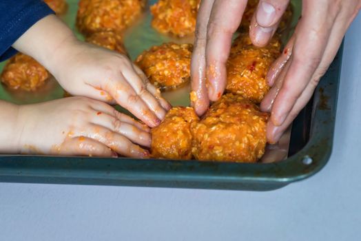Children and dad hands put the meatballs on a baking sheet