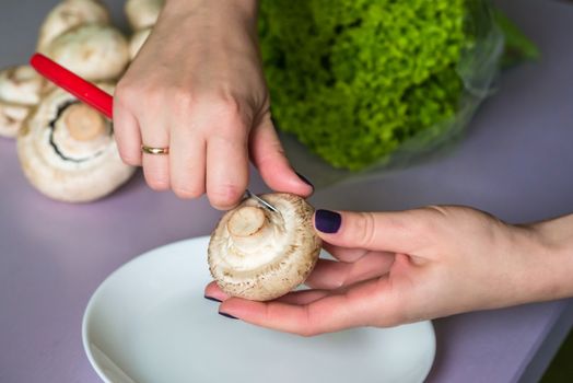 hands clean mushrooms with a knife over a white plate