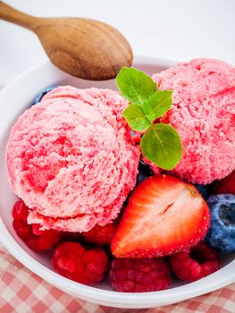 Close Up ice cream mixed berry fruits raspberry ,blueberry ,strawberry and peppermint leaves setup in white bowl on white wooden background . Summer and Sweet menu concept .