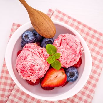 Close Up ice cream mixed berry fruits raspberry ,blueberry ,strawberry and peppermint leaves setup in white bowl on white wooden background . Summer and Sweet menu concept .