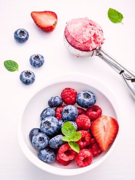 Close Up ice cream mixed berry fruits raspberry ,blueberry ,strawberry and peppermint leaves setup in white bowl on white wooden background . Summer and Sweet menu concept .