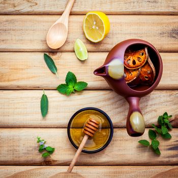 Herbal tea pot with fresh herbs sage ,peppermint ,dried indian bael, honey, lime and lemon on rustic wooden background flat lay.