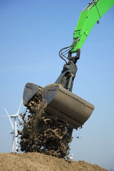 Green excavator scooping sand, putting it on a pile