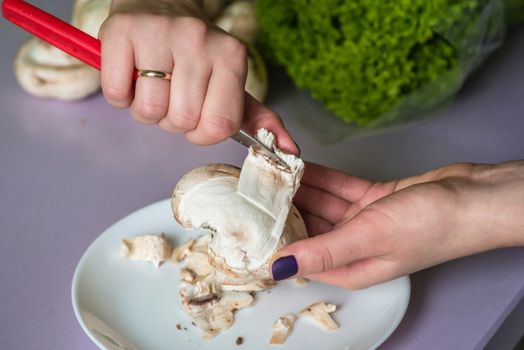 hands clean mushrooms with a knife over a white plate