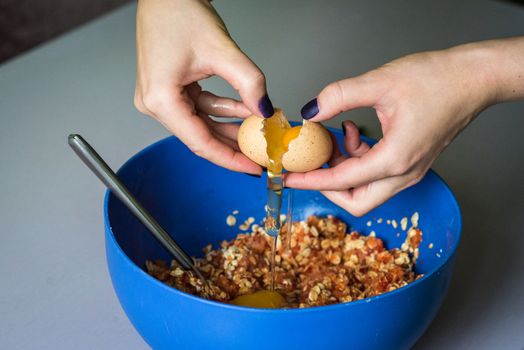 hand pours out raw egg of the shell in blue bowl