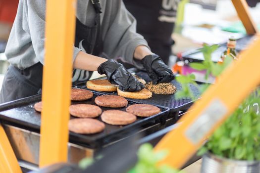 Chef making beef burgers outdoor on open kitchen international food festival event. Street food ready to serve on a food stall.