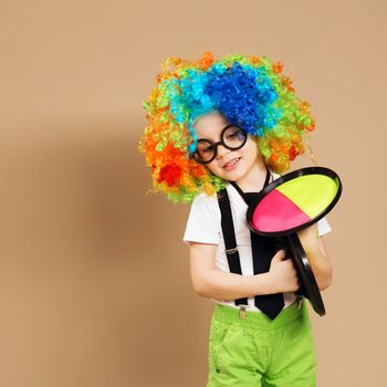 Blithesome children. Portrait of happy clown boy wearing large neon coloured wig. Kid in clown wig and eyeglasses playing catch ball game