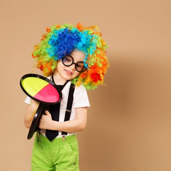 Blithesome children. Portrait of happy clown boy wearing large neon coloured wig. Kid in clown wig and eyeglasses playing catch ball game