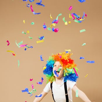 Little boy in clown wig jumping and having fun celebrating birthday. Portrait of a child throws up a multi-colored tinsel and confetti. Birthday boy. Positive emotions.