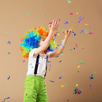 Little boy in clown wig jumping and having fun celebrating birthday. Portrait of a child throws up a multi-colored tinsel and confetti. Birthday boy. Positive emotions.