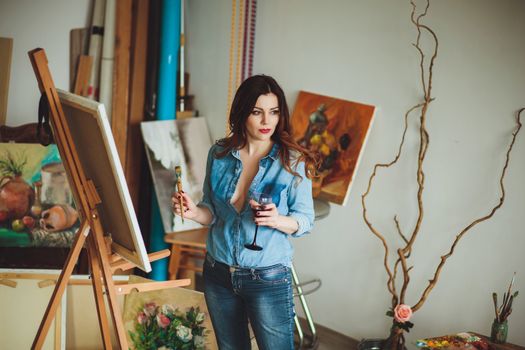 Woman artist painting a picture in a studio. Creative pensive painter girl paints a colorful picture on canvas with oil colors in workshop.