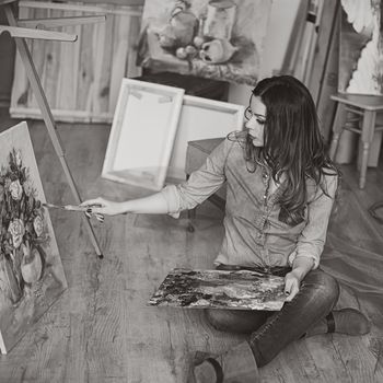 Woman artist painting a picture in a studio. Creative pensive painter girl paints a colorful picture on canvas with oil colors in workshop. black and white photography
