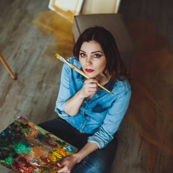 Woman artist painting a picture in a studio. Creative pensive painter girl paints a colorful picture on canvas with oil colors in workshop.