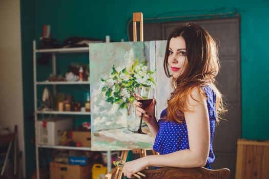 Woman artist painting a picture in a studio. Creative pensive painter girl paints a colorful picture on canvas with oil colors in workshop.