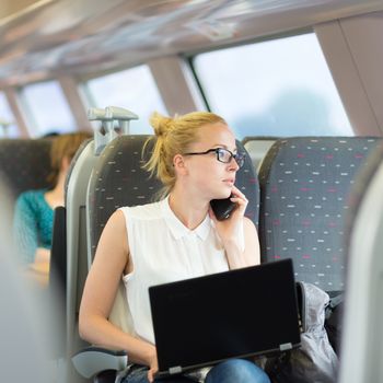 Businesswoman talking on cellphone and working on laptop while traveling by train. Business travel concept.