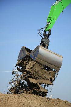 Green excavator scooping sand, putting it on a pile