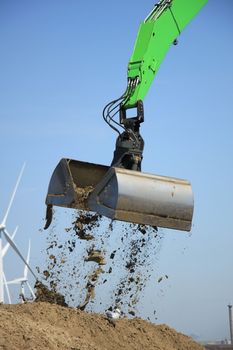 Green excavator scooping sand, putting it on a pile