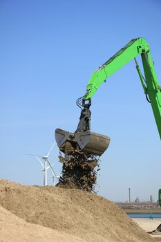 Green excavator scooping sand, putting it on a pile