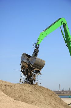 Green excavator scooping sand, putting it on a pile