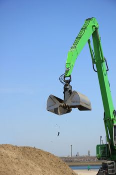 Green excavator scooping sand, putting it on a pile