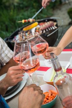 Happy friends having fun outdoors, Focus on hands toasting rose wine glass during barbecue