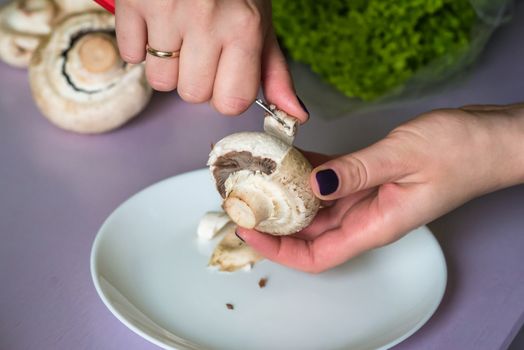 hands clean mushrooms with a knife over a white plate