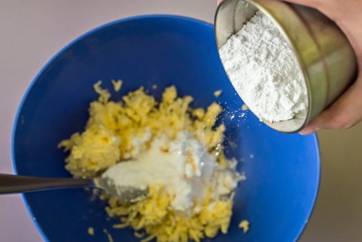 hand adds powdered sugar in butter over blue bowl