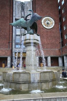 OSLO, NORWAY – AUGUST 18, 2016: Tourists around the main entrance of the Oslo City Hall with fountain of City Hall and clock in Oslo, Norway on August 18,2016.