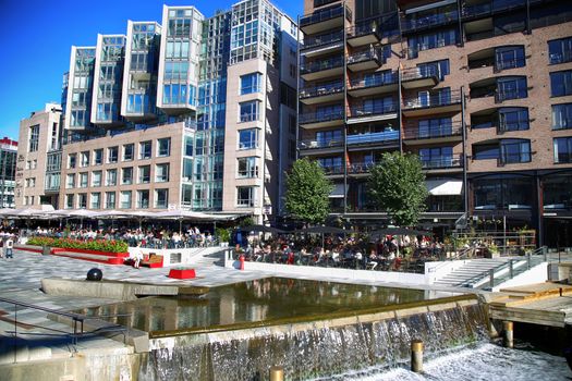 OSLO, NORWAY – AUGUST 17, 2016: People walking on wonderful modern residential district Aker Brygge with lux apartments, shopping, culture and restaurants in Oslo, Norway on August 17,2016.