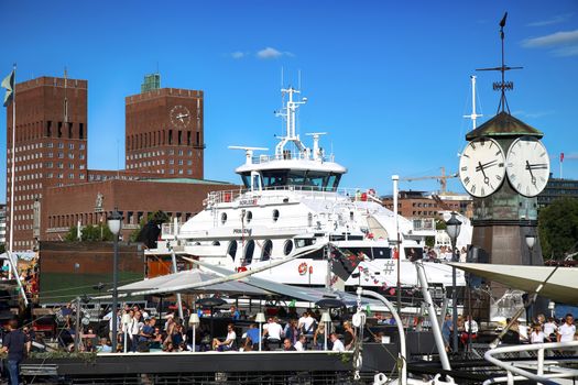 OSLO, NORWAY – AUGUST 17, 2016: People walking on modern district on street Stranden, Aker Brygge district and in the background is the City Hall in Oslo, Norway on August 17,2016.