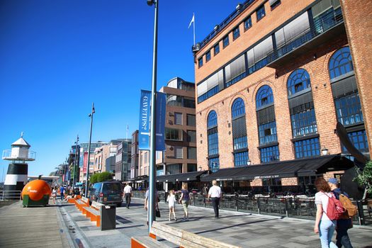 OSLO, NORWAY – AUGUST 17, 2016: People walking on modern district on street Stranden, Aker Brygge district with lux apartments, shopping, culture and restaurants in Oslo, Norway on August 17,2016.