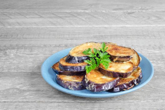 Fried eggplant on blue plate and grey wooden rustic background.
