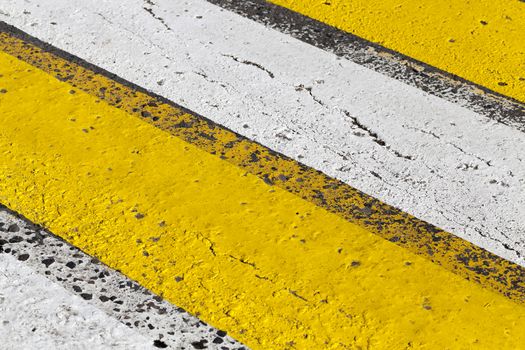 photographed close-up of road marking is located on the roadway, frayed yellow and white stripes of a pedestrian crossing