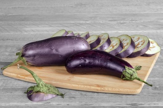 Eggplant lay on a cutting Board. Sliced and whole. Gray wood background, rustic.