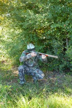 Camouflaged hunter in grassy area with sniper rifle looking through scope at target.