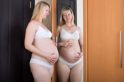 Pregnant woman holding belly in front of a mirror