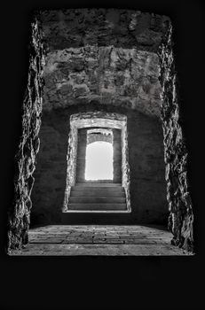 Black and white image of interior of an old basement with the sunlight's coming through the door over the stone walls and floor