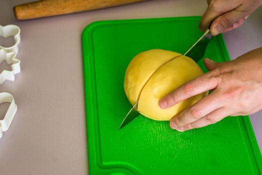 hand cuts the dough with a knife on green board